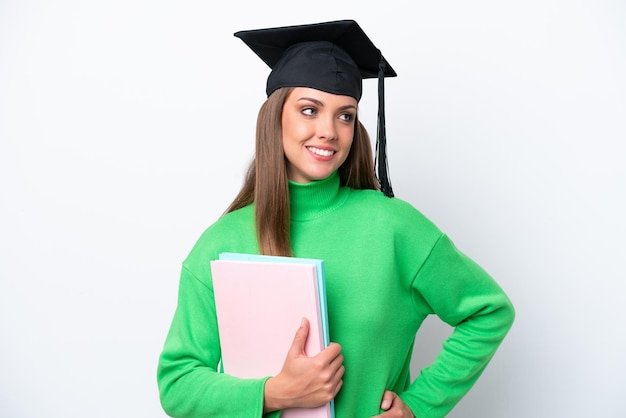 Young student caucasian woman isolated on white background posing with arms at hip and smiling