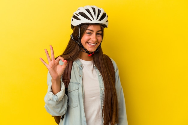 Young student caucasian woman wearing a bike helmet isolated on yellow background cheerful and confident showing ok gesture.