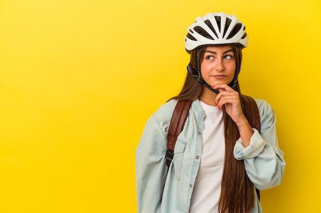 Young student caucasian woman wearing a bike helmet isolated on yellow background looking sideways with doubtful and skeptical expression.