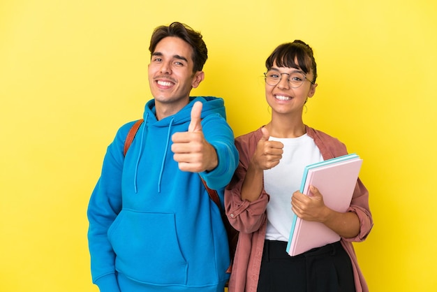 Young student couple isolated on yellow background giving a thumbs up gesture because something good has happened