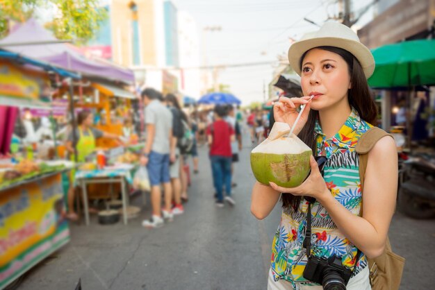 young student drinking fresh coconut water happiness on the market street land while travel vacation visiting Bangkok in Thailand with friend for graduation trip.