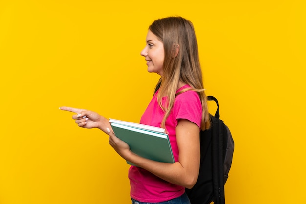 Young student girl over isolated yellow background pointing to the side to present a product