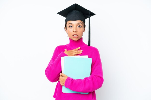 Young student hispanic woman holding a books isolated on white background surprised and shocked while looking right