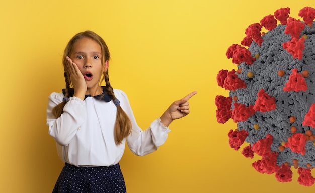 Young student is with shocked expression and indicates covid19 bacteria Yellow background