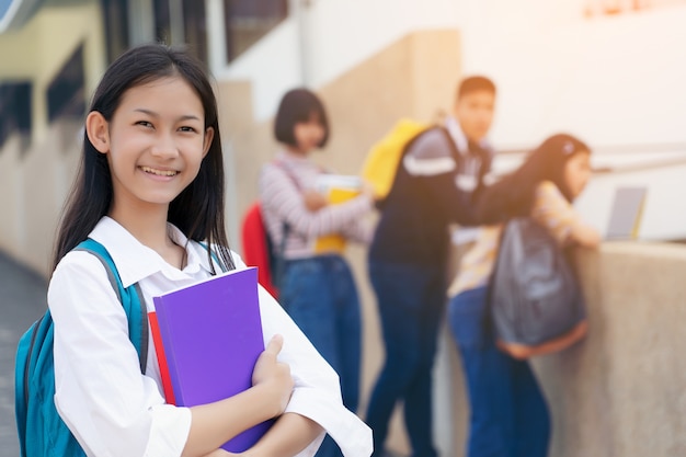 Young student teenager girl high school student carrying schoolbag holding notebooks with friends in background