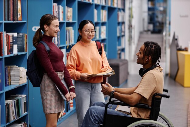 Photo young student with disability talking to friends in college library setting