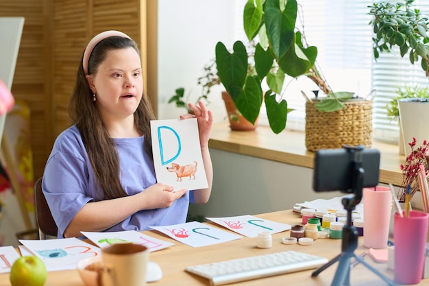 Young student with down syndrome learning letters in front of smartphone camera