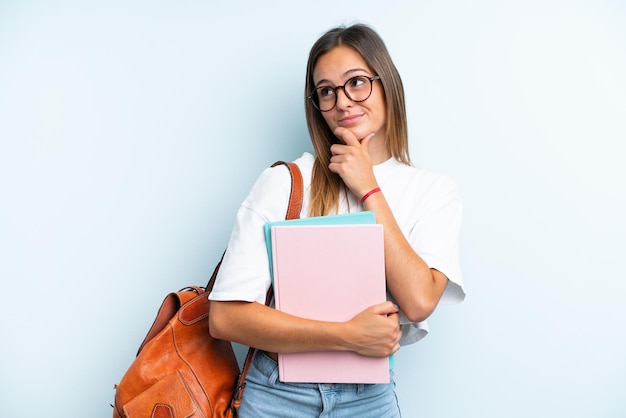 Young student woman isolated on blue background looking up while smiling