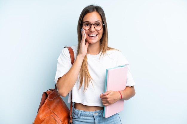 Young student woman isolated on blue background shouting with mouth wide open