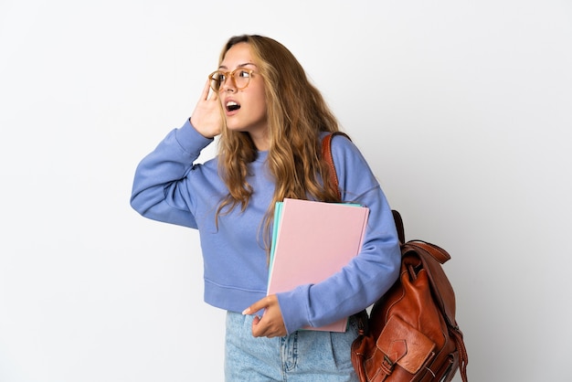 Young student woman isolated listening to something by putting hand on the ear