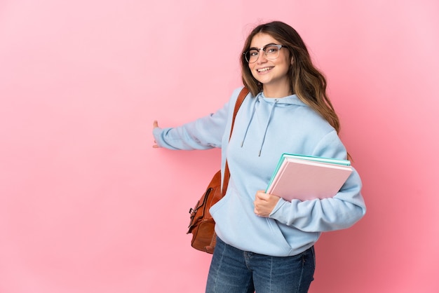 Young student woman isolated on pink wall extending hands to the side for inviting to come