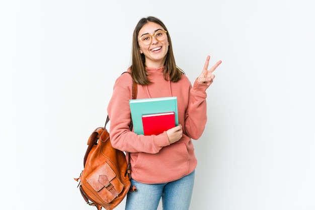 Young student woman isolated on white bakcground joyful and carefree showing a peace symbol with fingers.