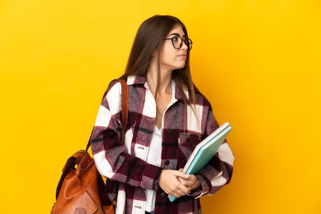 Young student woman isolated on yellow wall looking to the side