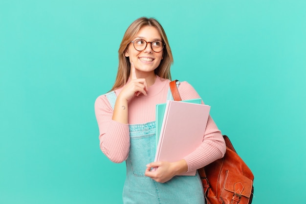 Young student woman smiling happily and daydreaming or doubting