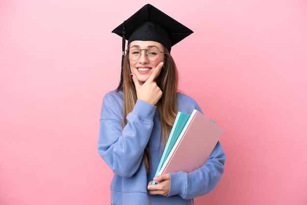 Young student woman wearing a graduate hat isolated on pink background happy and smiling