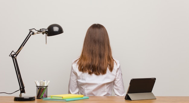 Young student woman working on her desk from behind, looking back