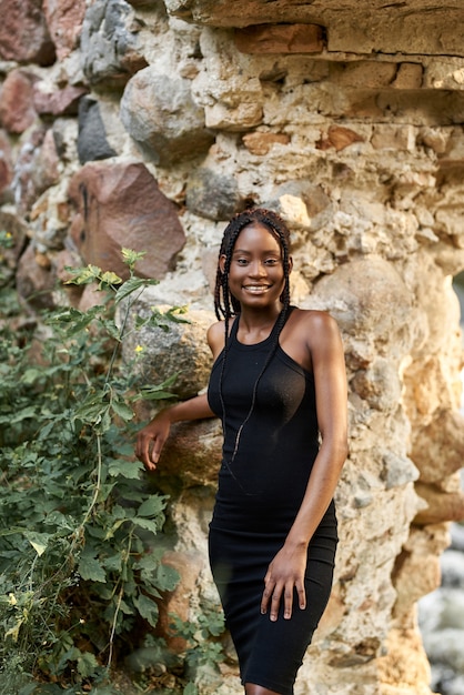 young stunning afro girl in black summer dress posing on the ruins in the forest