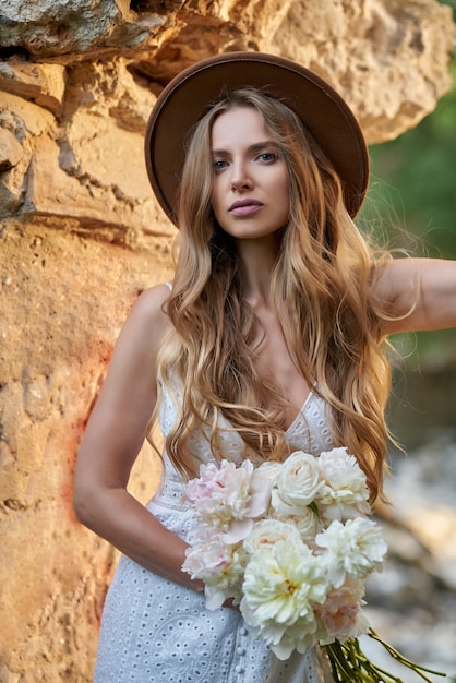 young stunning girl in a white summer dress and a hat with white peonies in her hands