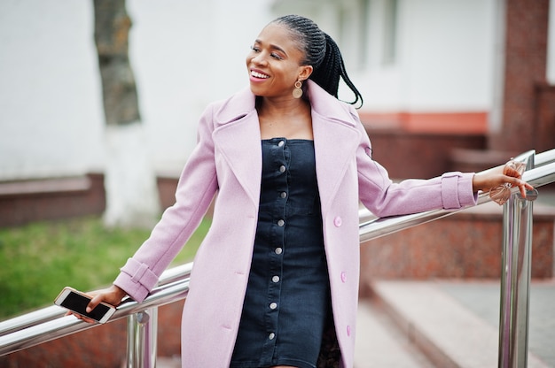 Young stylish beautiful african american woman in street, wearing fashion outfit coat, with mobile phone.