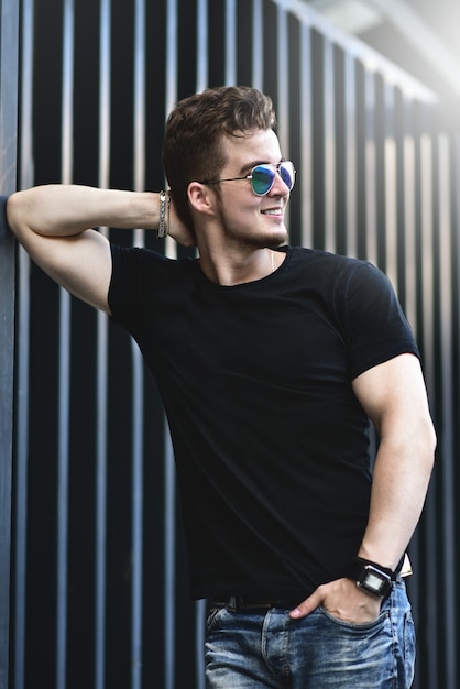 Young stylish and confident happy handsome guy model in t-shirt lifestyle in the street in sunglasses