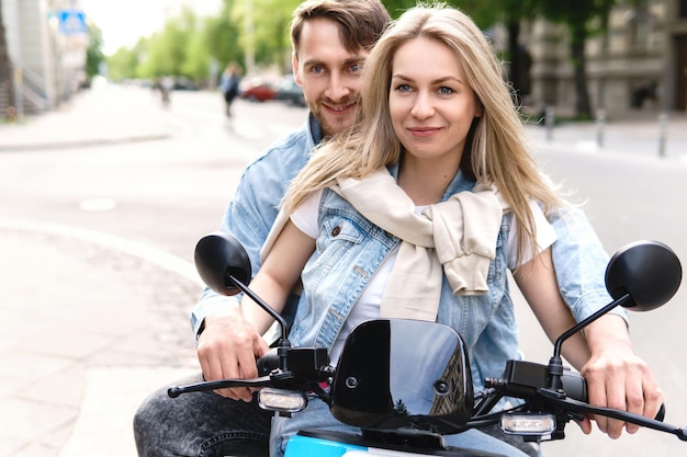 Young and stylish couple having fun while riding electric scooter on city street