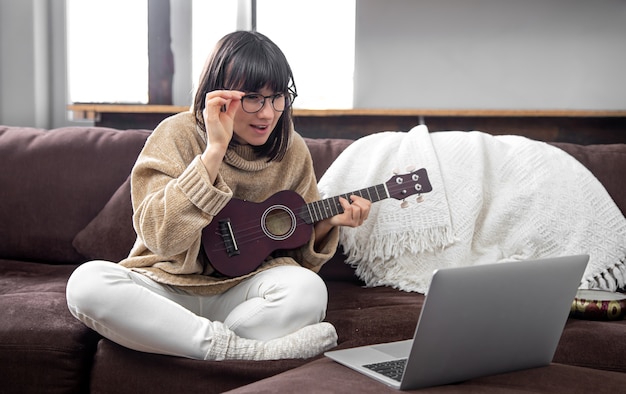 Young stylish girl with glasses learns to play the ukulele. online education, home education.