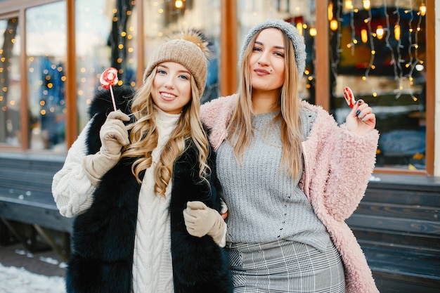 young and stylish girls in the winter clothes are walking in the solar city with sweets