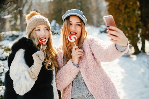 young and stylish girls in the winter clothes are walking in the solar park with candyes