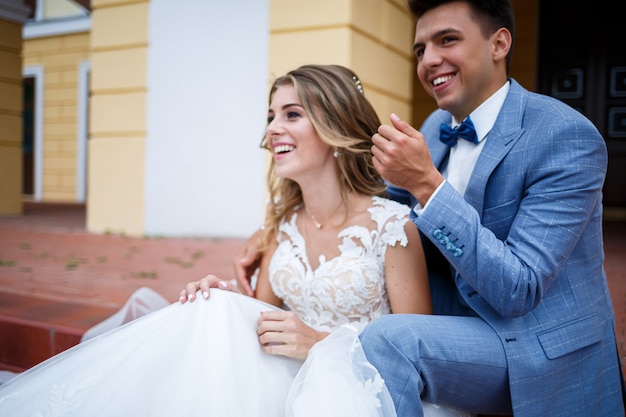 Young stylish guy in the costume of the groom and the bride beautiful girl in a white dress with a train walk in the park on their wedding day