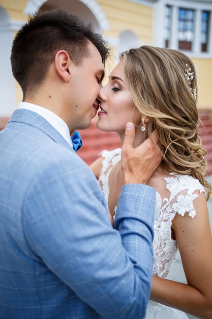 Young stylish guy in the costume of the groom and the bride beautiful girl in a white dress with a train walking on the background of a large house with columns on their wedding day