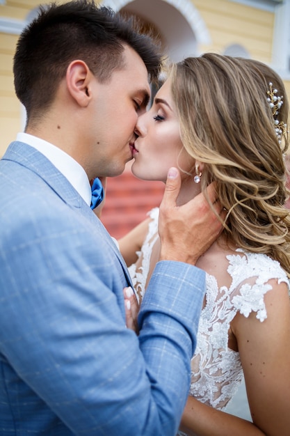 Young stylish guy in the costume of the groom and the bride beautiful girl in a white dress with a train walking on the background of a large house with columns on their wedding day