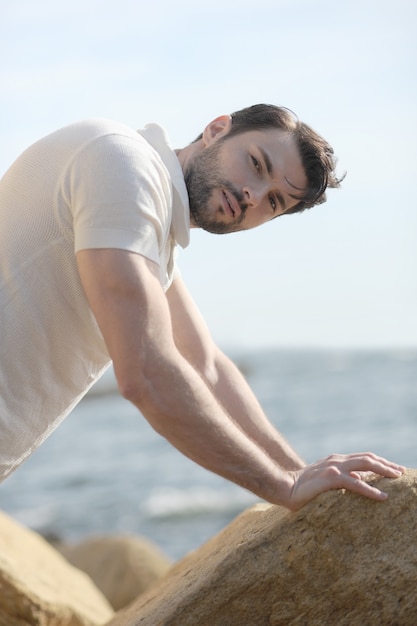 Photo young stylish man portrait near the sea dressed in white polo shirt