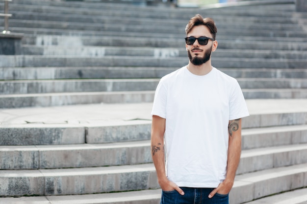 A young stylish man with a beard in a white T-shirt and glasses