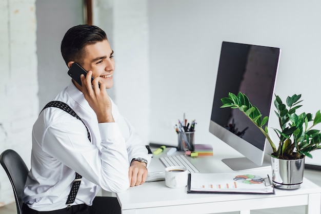 Young stylish man with a computer at the desk, isolated on white. Businessman in work.