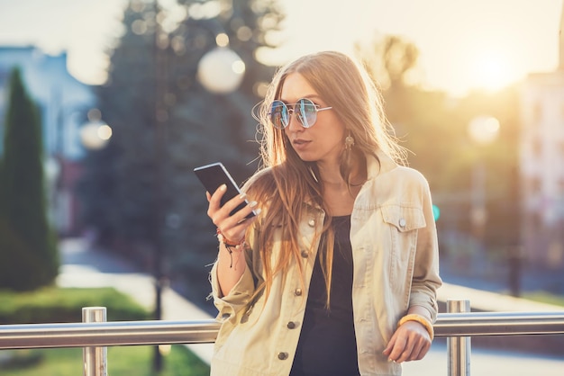 Young stylish pretty Woman hands holding a phone Sunset background Sunny daygood weather sunglasses cool accessories