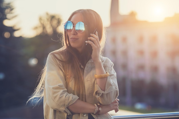 Young stylish pretty Woman hands holding a phone Sunset background Sunny daygood weather sunglasses cool accessories