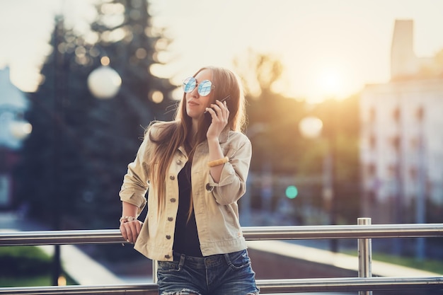 Young stylish pretty Woman hands holding a phone Sunset background Sunny daygood weather sunglasses cool accessories