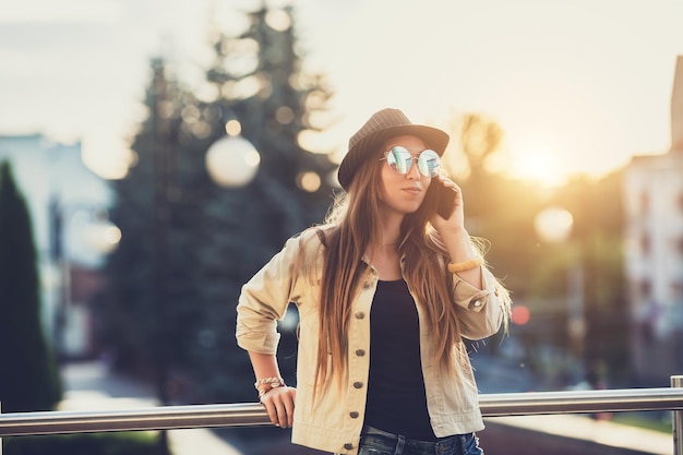 Young stylish pretty Woman hands holding a phone Sunset background Sunny daygood weather sunglasses cool accessories