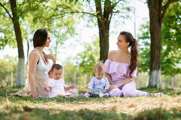 Young stylish trendy mothers sits with their daughters on the grass in a park.