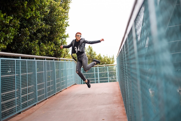 Young stylish wearing boy jumping on a bridge