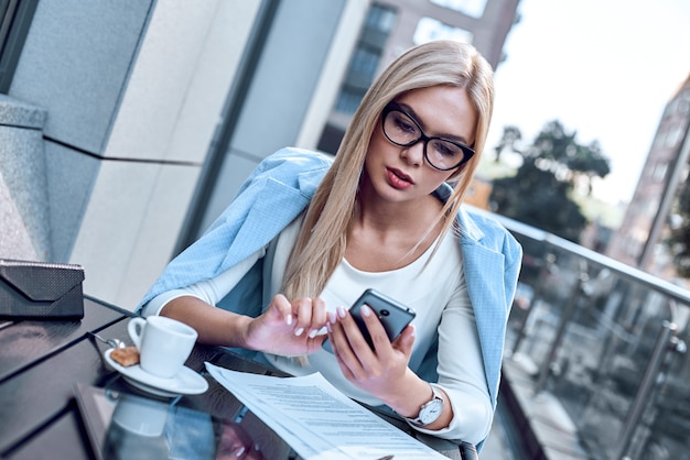 Young stylish woman chatting at smartphone in cafe