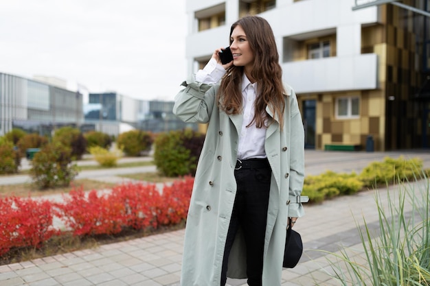 Young stylish woman in a coat with a hat talking on a mobile phone on the background of city