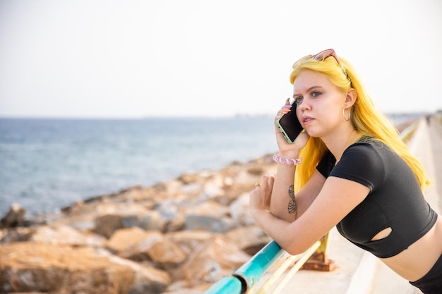 A young stylish woman communicates on a smartphone on the city embankment Rest and work in nature by the sea