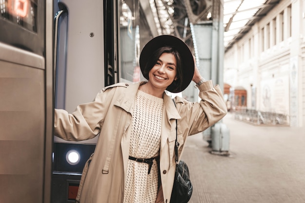 Young stylish woman hanging and smiling on the platform of a train carriage