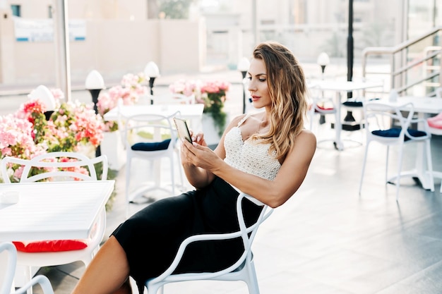 Photo a young stylish woman sits in a street cafe and uses her phone to exchange messages