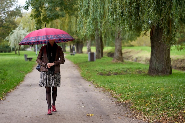 Young stylish woman walking in the autumn park with huge red umbrella