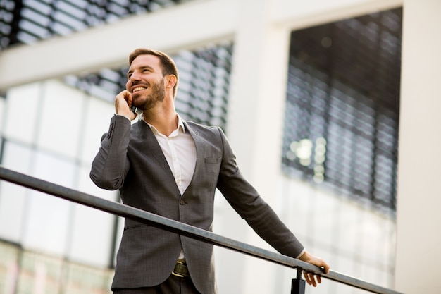 Young successful businessman wearing grey suit and holding his smartphone while standing near modern