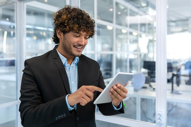 Young successful businessman with tablet computer smiling hispanic man working inside a modern