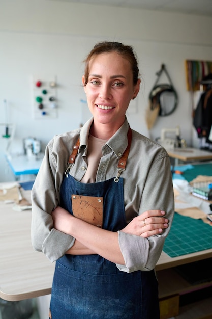 Young successful female leather worker in apron looking at camera