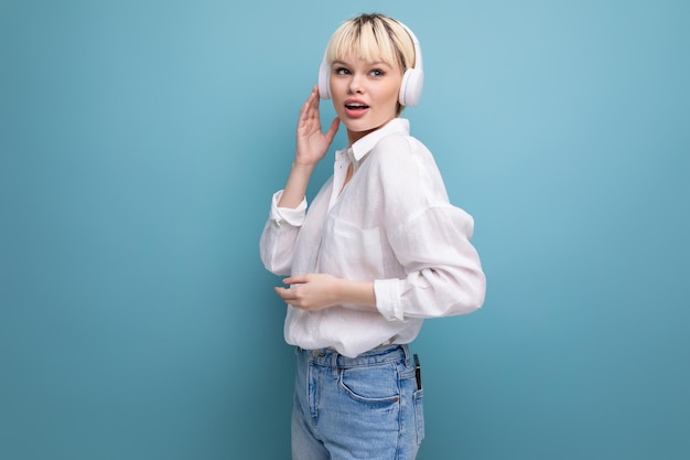 Young successful pretty blond office worker woman in a white shirt and jeans uses headphones during